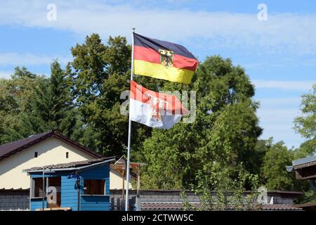 Halbe, Deutschland. September 2020. Die Flagge des Landes Brandenburg und die Flagge der Bundesrepublik Deutschland mit dem Adler auf schwarz-rot-goldenen Streifen wehen über einem Garten auf einem Mast. Quelle: Soeren Stache/dpa-Zentralbild/ZB/dpa/Alamy Live News Stockfoto