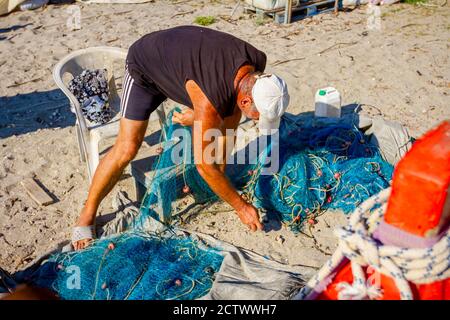 Fischer häufen Fischnetz auf dem Sandstrand und bereiten sich auf sein nächstes Angeln. Stockfoto