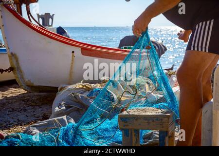 Fischer häufen Fischnetz und bereiten sich auf sein nächstes Angeln. Die Boote sind trocken am Sandstrand angedockt. Stockfoto