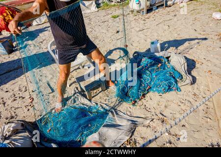 Fischer häufen Fischnetz auf dem Sandstrand und bereiten sich auf sein nächstes Angeln. Stockfoto