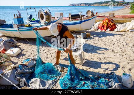 Fischer häufen Fischnetz und bereiten sich auf sein nächstes Angeln. Die Boote sind trocken am Sandstrand angedockt. Stockfoto