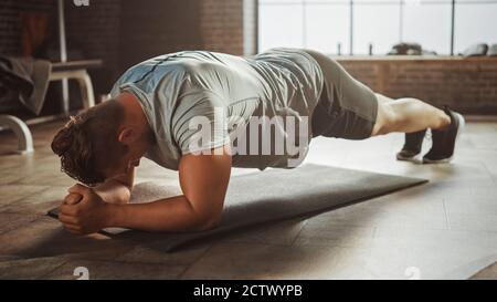 Starker männlicher Mann hält eine Plank-Position, um seine Kernkraft auszuüben. Der Mensch ist erschöpft und kämpft mit der Ausbildung. Workout in einem Stockfoto