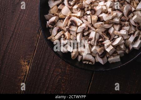 Leckere gehackte Champignon-Pilze in der Pfanne, ungekochte Speisen in Scheiben geschnitten, dunkelbrauner Holzhintergrund, Draufsicht Stockfoto
