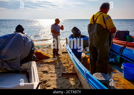 Zwei Fischer am Strand, einer im Boot und der andere neben dem Boot, stapeln Fischnetz für das nächste Angeln. Stockfoto