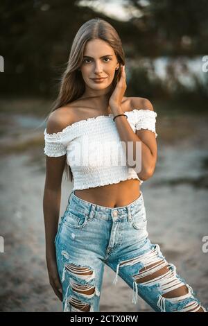 Hübsches Mädchen posiert auf Sand in weißen Top und blaue Jeans. Sie berührt ihr Haar am Ohr und schaut in die Kamera. Hochwertige Fotos Stockfoto