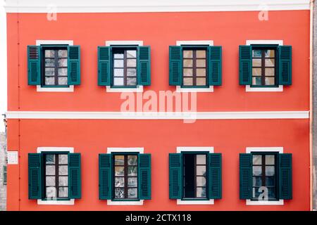 Ein helles rosa Haus mit braunen Fensterrahmen und offenen grünen Fensterläden. Stockfoto