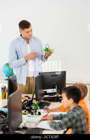 Selektiver Fokus des Lehrers, der auf Roboter in der Nähe von multiethnischen Schülern zeigt Und Computern Stockfoto