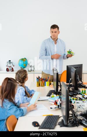 Selektiver Fokus des Lehrers zeigt auf Roboter in der Nähe von Schülerinnen und Computer im Klassenzimmer Stockfoto