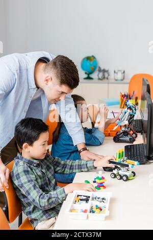 Selektiver Fokus des Lehrers, der in der Nähe multiethnischer Schüler steht, die Roboter modellieren Im Klassenzimmer Stockfoto