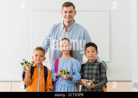 Lehrer umarmt multikulturelle Schüler mit Robotern in der MINT-Schule Stockfoto