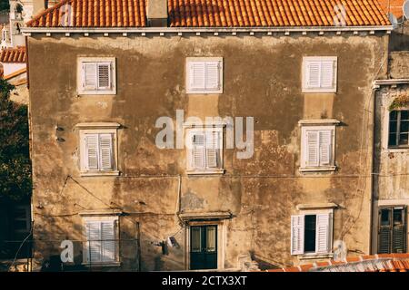 Ein graues dreistöckiges Haus mit weißen Fensterläden und orangefarbenen Fliesen auf dem Dach. Stockfoto