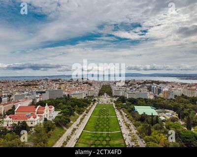 Blick über die Drohne auf den Eduardo VII Park in Lissabon, Portugal, mit geometrischen Gärten und der Skyline der Stadt im Hintergrund. Stockfoto