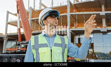 Futuristischer Architekturingenieur mit Augmented Reality-Headset und Gesten zur Steuerung der industriellen Baustellenbaustelle. Zoll Stockfoto