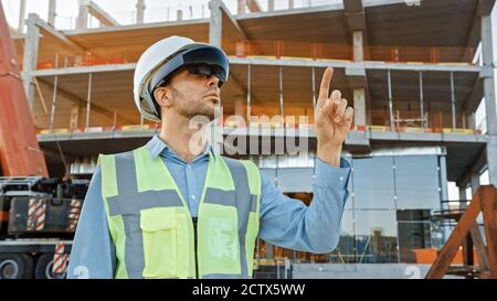 Futuristischer Architekturingenieur mit Augmented Reality-Headset und Gesten zur Steuerung der industriellen Baustellenbaustelle. Zoll Stockfoto