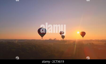 Luftdrohne Ansicht der bunten Heißluftballons fliegen über grünen Park und Fluss in der kleinen europäischen Stadt bei Sommersonnenaufgang, Kiew Region, Ukraine Stockfoto