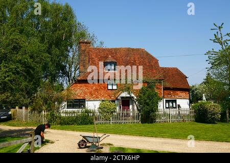 Man Gartenarbeit vor Manor Farm Cottage, ein kleines Bauernhaus aus dem 17. Jahrhundert neben dem Wealdway Fernwanderweg, Lower Haysden, Kent, England Stockfoto