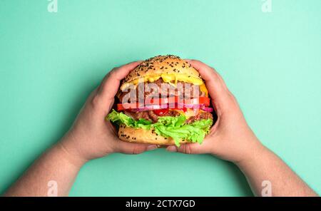 Oben mit Hamburger, der mit beiden Händen auf einem grünen Tisch gehalten wird. Blick von oben mit einem hausgemachten Rinderburger. Stockfoto