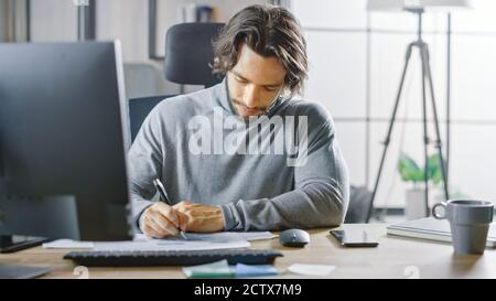 Schöner langhaariger Unternehmer sitzt an seinem Schreibtisch im Büro arbeitet auf Desktop-Computer, arbeiten mit Dokumenten, Charts, Grafiken, Statistik und Stockfoto