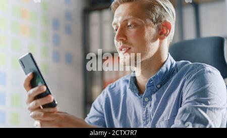 Unternehmer sitzt an seinem Schreibtisch arbeitet im stilvollen Büro, mit Smartphone, nutzt Social Media App, E-Mail-Geschäftspartner, Messaging. Stockfoto