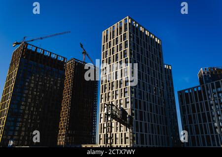 Wohnungsentwicklung. Moderne Hochhäuser im Bau und Kräne vor dem klaren blauen Himmel. Städtischer Hintergrund. Konzept der Zersiedelung Stockfoto