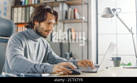 Schöner langhaariger hispanischer Geschäftsmann, der an seinem Schreibtisch im Büro sitzt, arbeitet auf einem Laptop. Kreative Entwicklung Neuer Software Unicorn Startup Stockfoto
