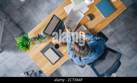Geschäftsmann sitzt an seinem Schreibtisch im Büro verwendet Laptop-Computer, arbeiten mit Company Strategy Documents, Correcting Charts, Zeichnung Grafiken und Stockfoto