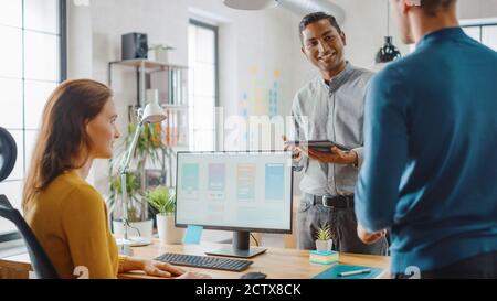 Drei Mobile Software-Entwickler arbeiten an Desktop-Computer, sie diskutieren Smartphone Application Design verwenden Touch Screen Digital Tablet. Modern Und Stilvoll Stockfoto