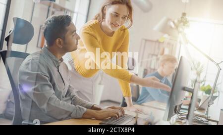 Handsome Indian Professional sitzt an seinem Schreibtisch Arbeiten auf Laptop-Computer, Young Beautiful Team Leader gibt Ratschläge über Projekt-Details. Büro Stockfoto
