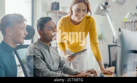 Talentierter Unternehmer, der an seinem Desktop-Computer arbeitet, mit Projektmanager und Teamleiter, die neben ihm stehen, haben Diskussion, Problem finden Stockfoto
