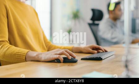 Anonyme junge Frau sitzt an ihrem Schreibtisch mit Laptop-Computer. Konzentrieren Sie sich auf Hände mit Maus und Tastatur. Im Hintergrund Bright Office wo Stockfoto