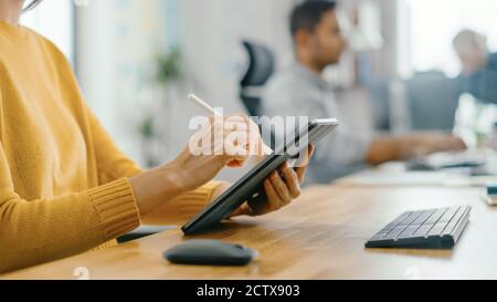 Anonyme junge Frau sitzt an ihrem Schreibtisch Sie zeichnet, schreibt und benutzt Stift mit digitalem Tablet-Computer. Konzentrieren Sie sich mit dem Stift auf die Hände. Helles Büro Stockfoto