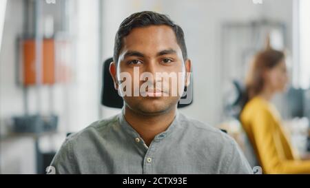 Porträt eines gutaussehenden professionellen indischen Mann an seinem Schreibtisch, Blick auf die Kamera. Erfolgreicher Mann, der in Bright Diverse Office arbeitet. Stockfoto