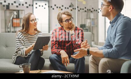 Junge Frau und zwei männliche Kollegen bei einem freundlichen Treffen und Diskussion über neue Geschäftsideen. Lockere Coworking Atmosphäre im Loft Office Stockfoto