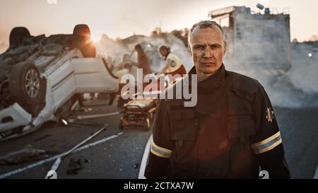 Portrait des tapferen Feuerwehrmann, der zur Kamera geht. Im Hintergrund mutige Helden Sanitäter und Feuerwehrleute Rettungsteam kämpfen Feuer, Rauch und retten Stockfoto
