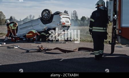 Rettungsteam von Feuerwehrleuten und Sanitätern arbeiten an einer schrecklichen Auto Crash Verkehr Unfallszene. Ausrüstung Vorbereiten, Strecken, Erste Hilfe. Speichern Stockfoto