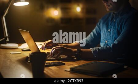 Anonymer Mann sitzt an seinem Schreibtisch im Office Studio und arbeitet am Abend auf einem Laptop. Mann, der mit Daten arbeitet, Statistiken analysieren. Stockfoto