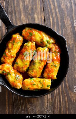 Nahaufnahme von Kohlröllchen gefüllt mit Hackfleisch, Reis und gebacken mit Tomatensauce in Bratpfanne über Holzhintergrund. Draufsicht, flach liegend Stockfoto