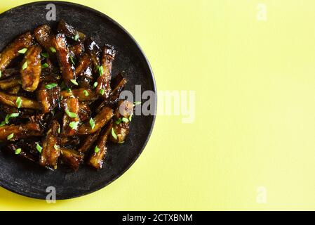 Nahaufnahme der Rührbraten Bulgogi Aubergine auf Platte über gelbem Hintergrund mit freien Text Raum. Gebratene Aubergine im koreanischen Stil. Draufsicht, flach liegend Stockfoto