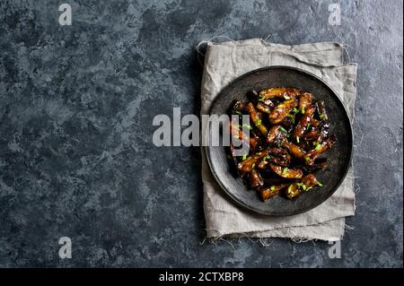 Rührbraten Bulgogi Aubergine auf Platte über dunklem Steinhintergrund mit freiem Textraum. Gebratene Aubergine im koreanischen Stil. Draufsicht, flaches Lay Stockfoto