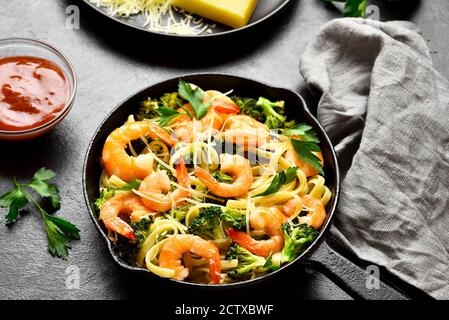 Garnelen und Brokkoli Pasta in Gusseisen Pfanne über dunklen Stein Hintergrund. Leckeres gesundes Gericht zum Abendessen. Nahaufnahme Stockfoto