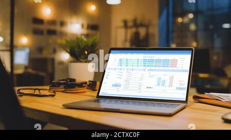 Laptop on the Desk in the Office zeigt Unternehmenswachstumsdaten mit Grafiken, Diagrammen und Software-UI. Im Hintergrund stilvolles modernes Office Studio im Stockfoto
