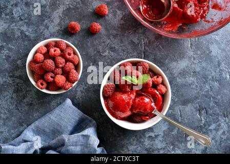 Himbeer-Sorbet, Eisportionierer mit frischen Beeren in Schüssel auf blauem Stein Hintergrund. Leckeres sommerliches kaltes Dessert. Draufsicht, flach liegend Stockfoto