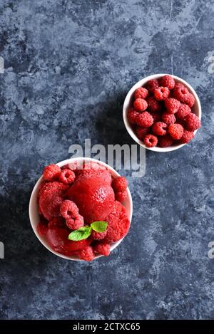 Himbeer-Sorbet, Eisportionierer mit frischen Beeren in Schale über blauem Stein Hintergrund mit Freitext Raum. Leckeres sommerliches kaltes Dessert. Draufsicht, FLA Stockfoto