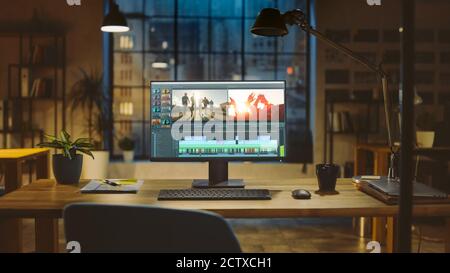 Aufnahme eines Desktop-Computers, der auf einem Schreibtisch mit professioneller Videomontage-Bearbeitungssoftware steht. Im Hintergrund warme Abendbeleuchtung und Open Space Stockfoto