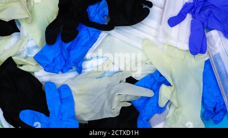 Mehrfarbige krümelige Latex-OP-Handschuhe und medizinische Schutzmasken liegen in Unordnung. Flach liegend. Mittel gegen das Covid-19-Virus. Stockfoto