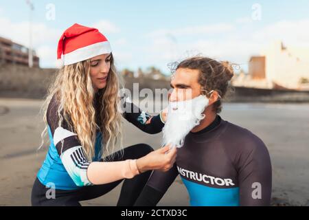 Paar am Strand helfen sich gegenseitig, sich zu verkleiden Als Weihnachtsmann Stockfoto