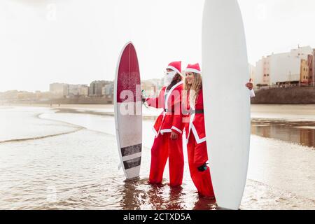 Ein Paar als weihnachtsmann am Strand mit gekleidet Ihre Surfbretter Stockfoto