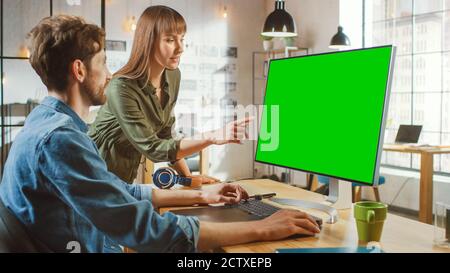 Weibliche Art Director berät Designer-Kollegen, sie arbeiten an einem Personal Computer mit Green Screen Mock Up Display. Sie arbeiten in einem Cool Office Loft Stockfoto