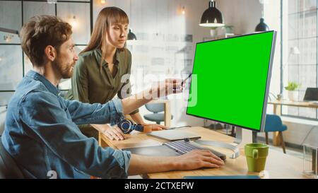 Weibliche Art Director berät Designer-Kollegen, sie arbeiten an einem Personal Computer mit Green Screen Mock Up Display. Sie arbeiten in einem Cool Office Loft Stockfoto