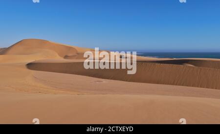 Große beigefarbene Sanddünen mit Atlantikküste im Hintergrund bei Swakopmund, Namib Wüste, Namibia, Afrika. Stockfoto